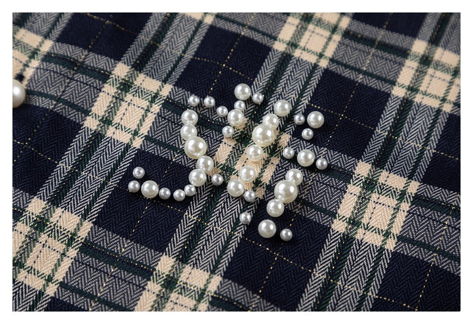 Close-up of pearl-like decorative beads arranged on navy and cream plaid fabric.