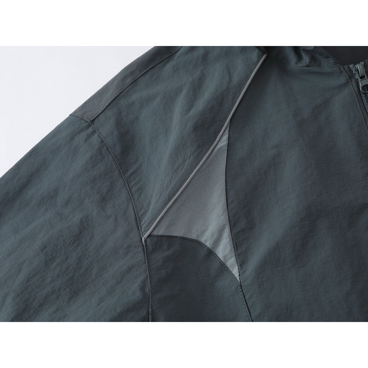 Close-up of a dark gray jacket's sleeve and side panel with light gray piping and an inset panel.