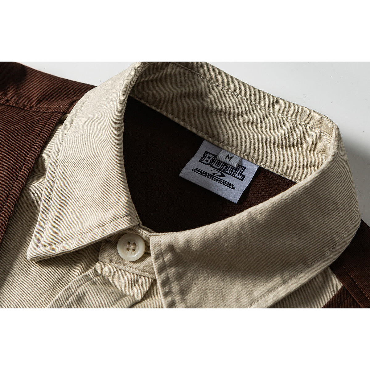 Close-up of a beige and dark brown jacket collar with a button and sewn-in neck label.