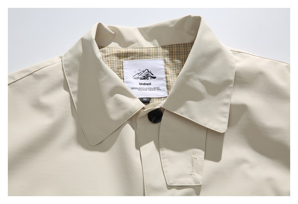 Close-up of a cream garment collar, dark button, plaid lining, and sewn-in Undrest label.