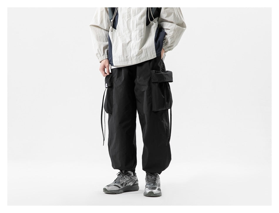 Front view of black wide-leg cargo pants with side flap pockets and cuffed ankles, worn with gray sneakers
