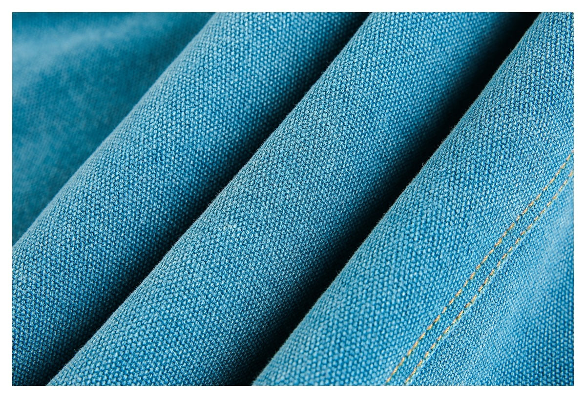 Close-up of folded blue woven fabric showing its textured surface and a line of golden-orange stitching.