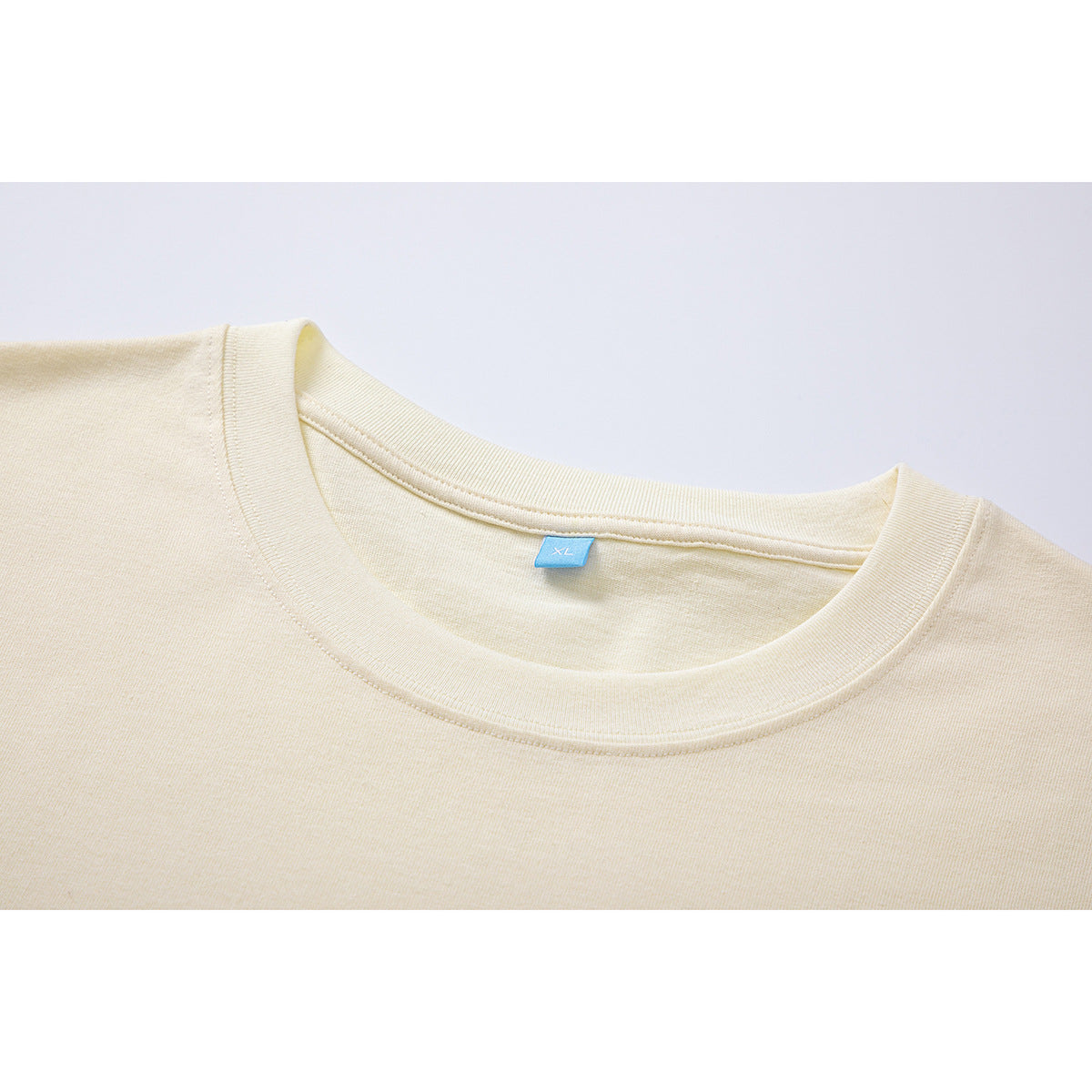 Close-up of a cream T-shirt's ribbed crew neckline and small blue XL neck label.