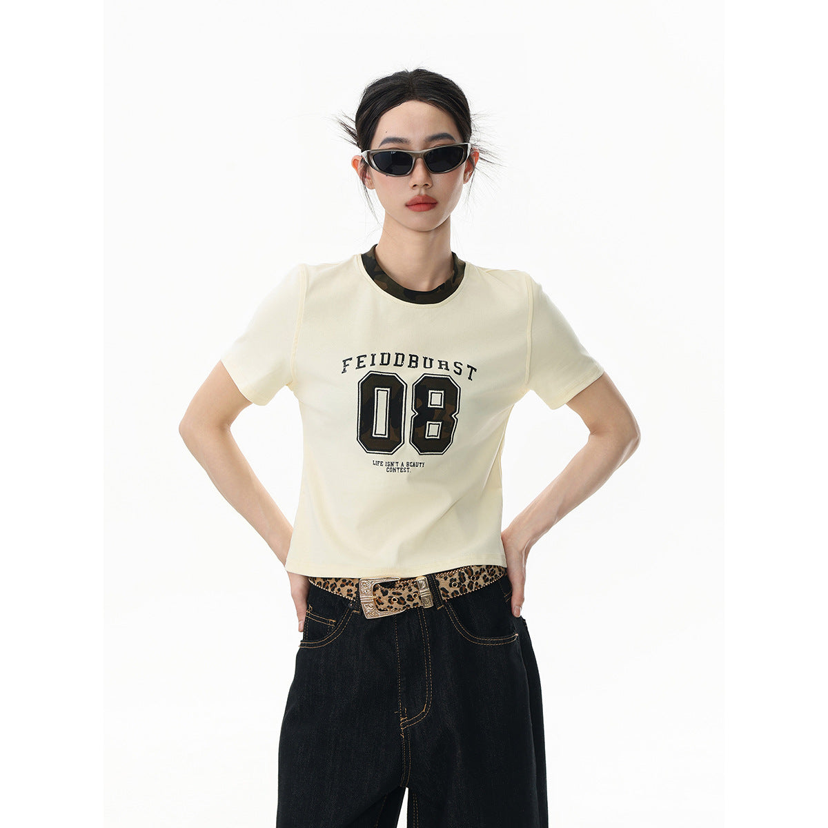 Model wearing an ivory graphic T-shirt with dark wide-leg jeans and a leopard-print belt, shown from the front.