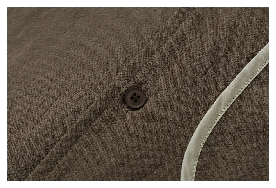 Close-up of a dark button, brown shirt fabric, and pale contrasting edge trim.