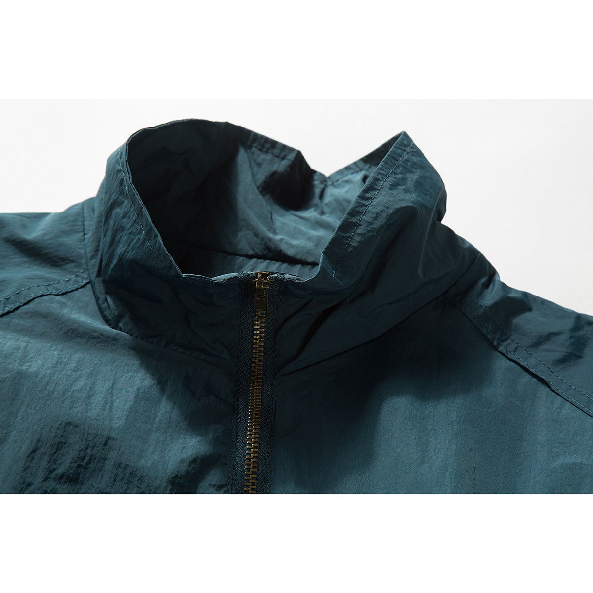 Close-up of a dark teal jacket's tall collar and brass-tone front zipper.