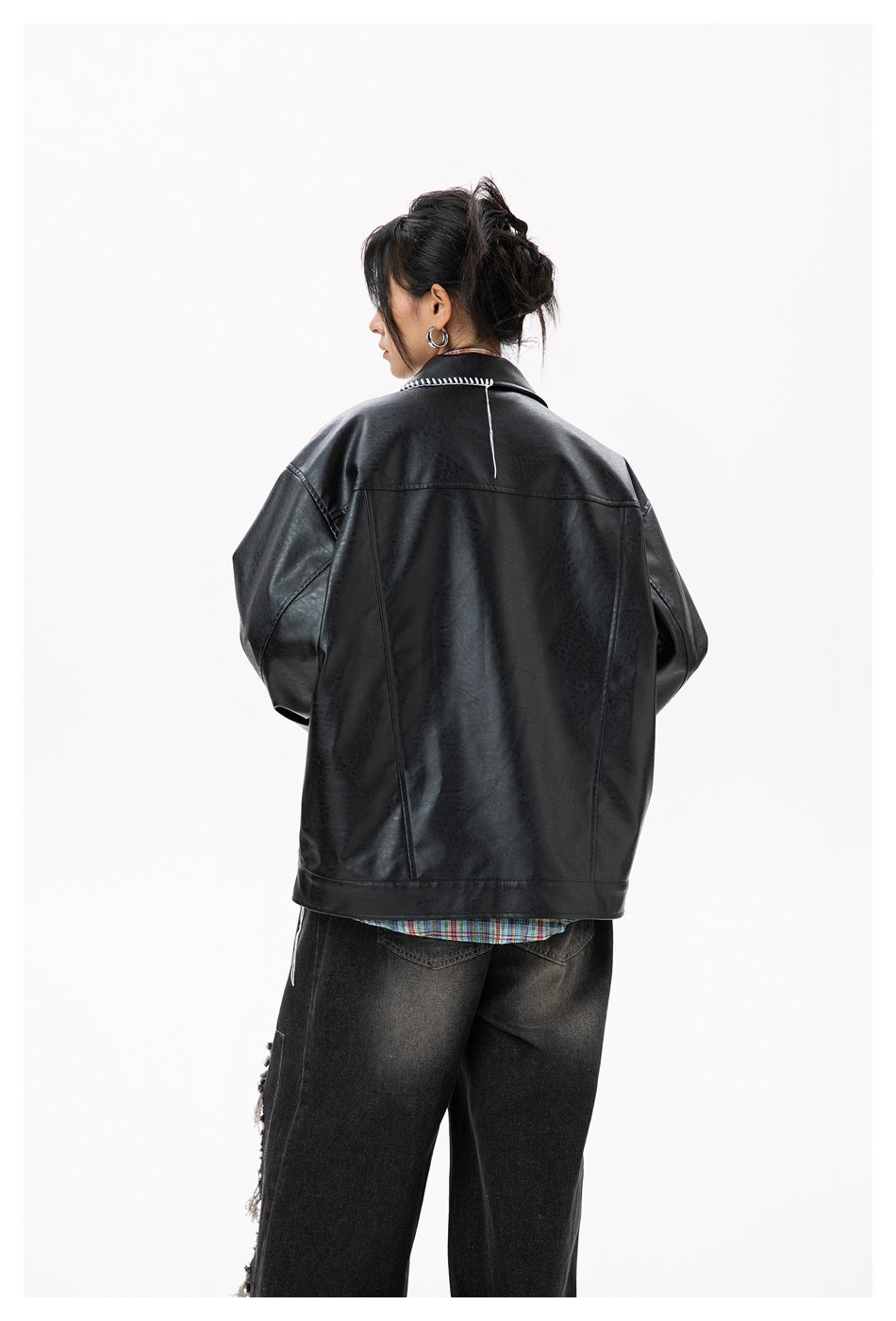 Back view of a model wearing a black leather-look jacket with white stitched collar edge and plaid shirt