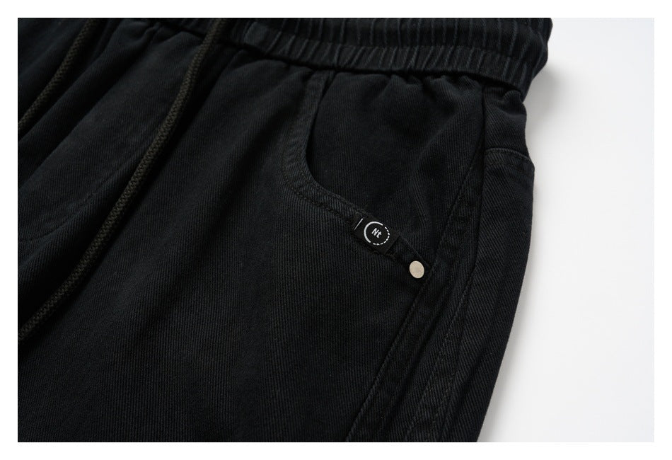 Close-up of a black pants side pocket with a small sewn tab and metal rivet.