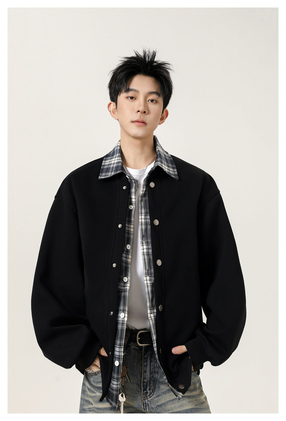 Model wearing an oversized black snap-front jacket over a gray plaid shirt and white tee.