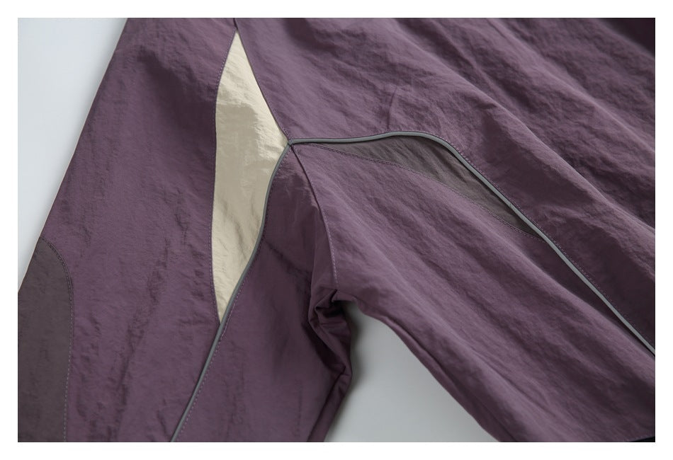 Close-up of plum garment color-block panels, cream inset, and gray piping along the leg.