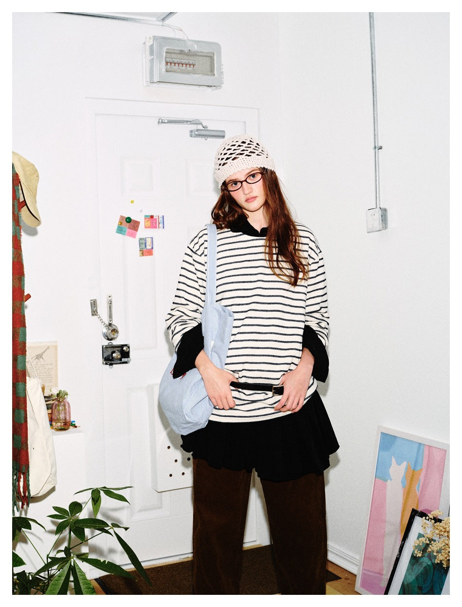 Closer view of a model in a loose cream shirt with thin dark stripes and black cuffs, layered over a black skirt.