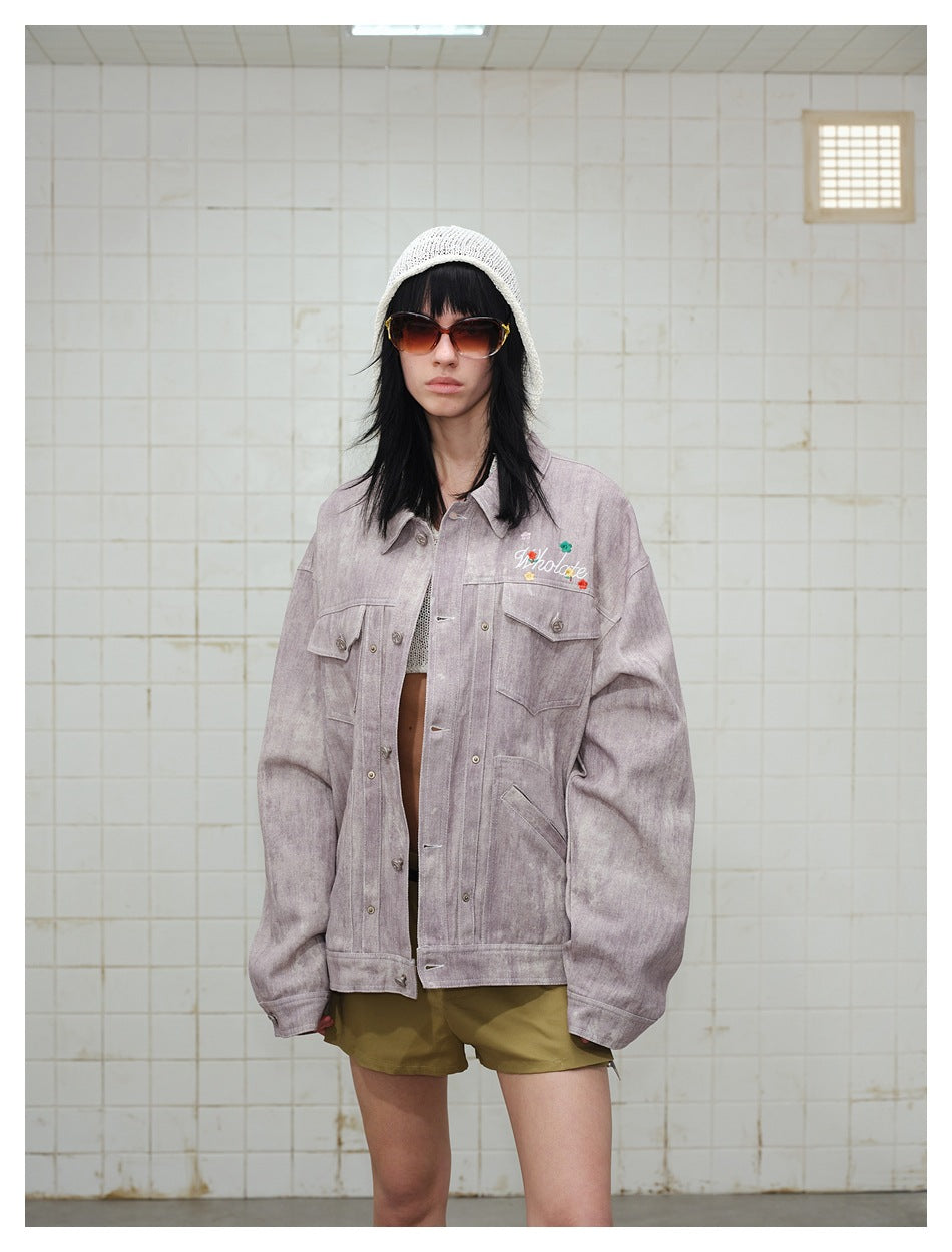 Model wearing a mauve washed button-front jacket with embroidered floral lettering, paired with olive shorts and a white knit