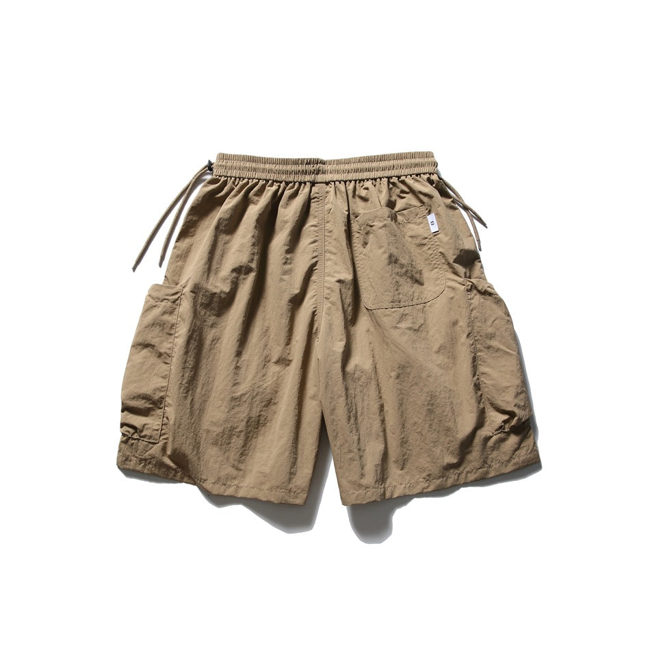 Taupe shorts with an elastic drawstring waist, patch pockets, and oversized side cargo pockets.
