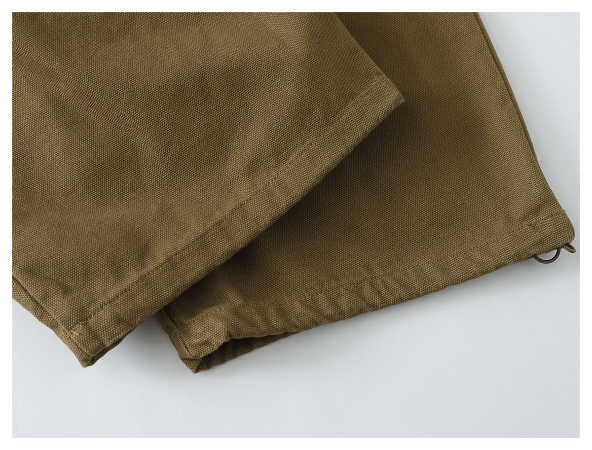 Close-up of overlapping olive-brown trouser hems with stitched edges and small metal loops.