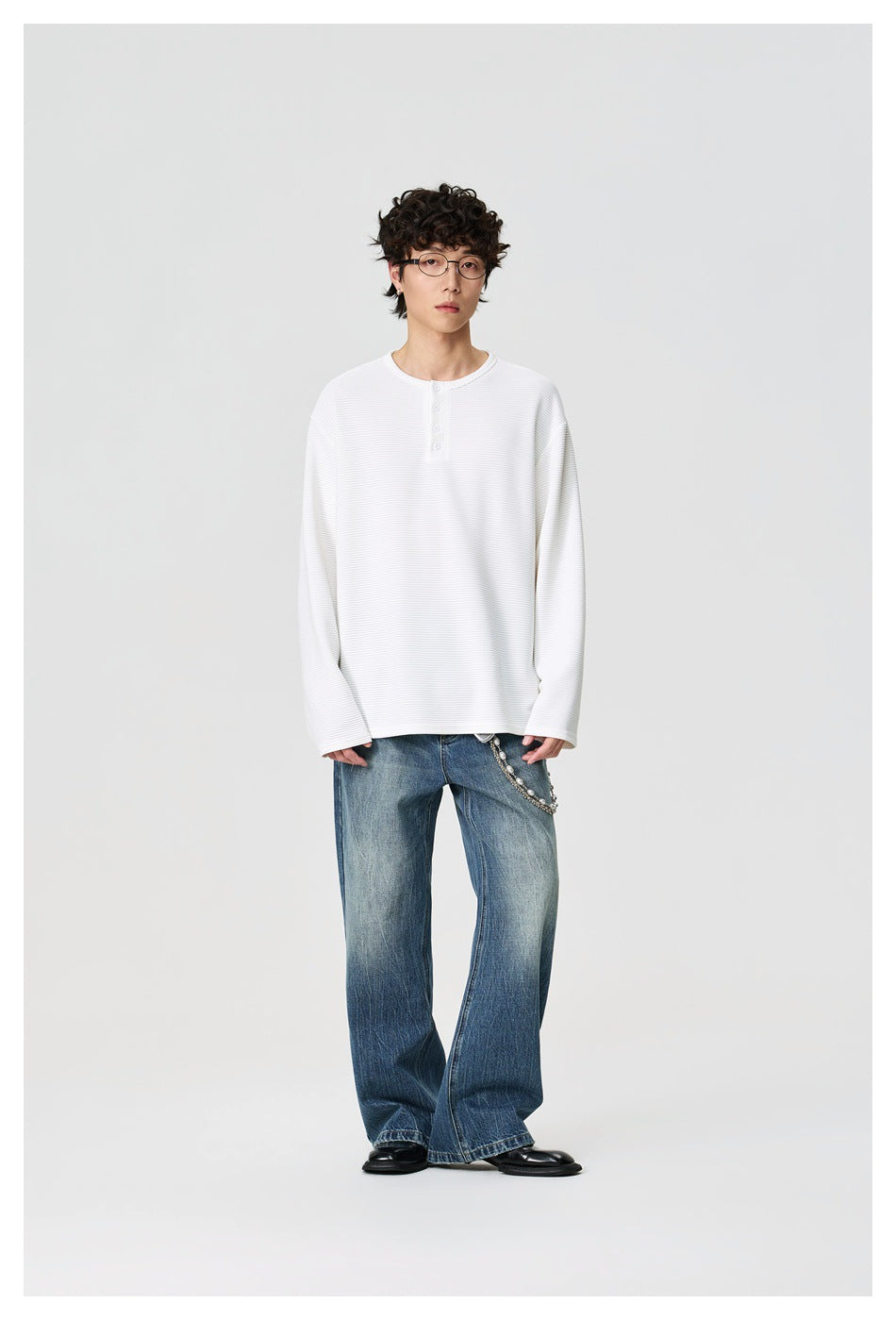 Full-length front view of a model wearing a white ribbed henley shirt with loose blue jeans.
