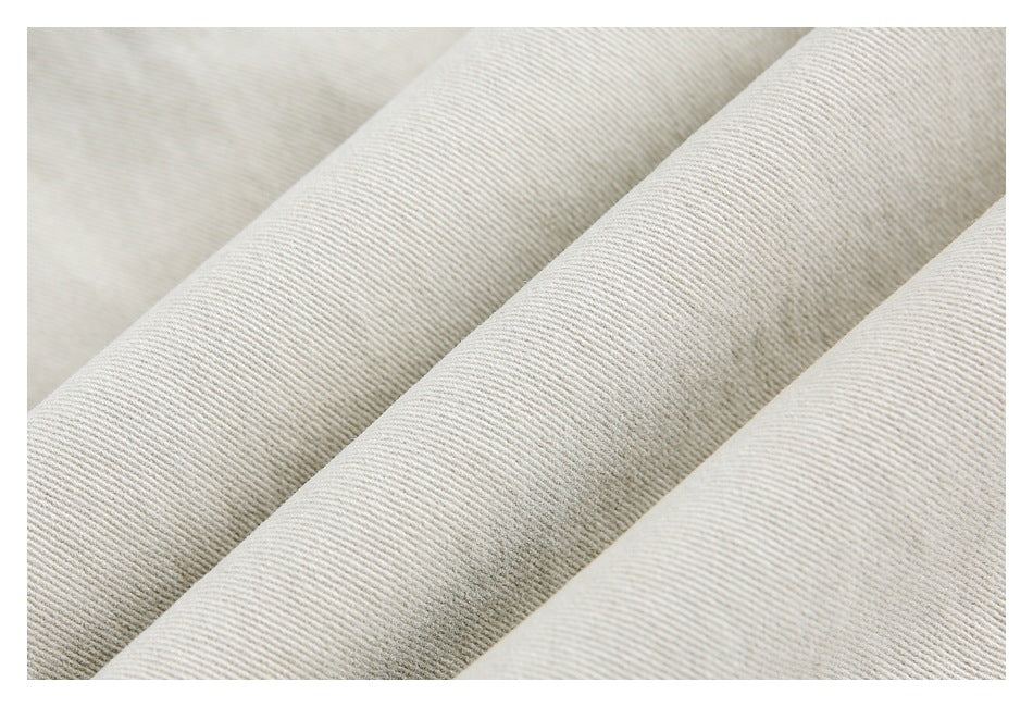 Close-up of light beige diagonally ribbed denim fabric folded into soft ridges.