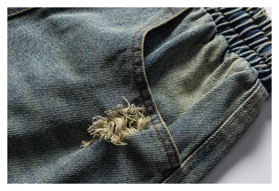 Close-up of blue washed denim with orange stitching, a frayed distressed patch, and gathered elastic at the edge.