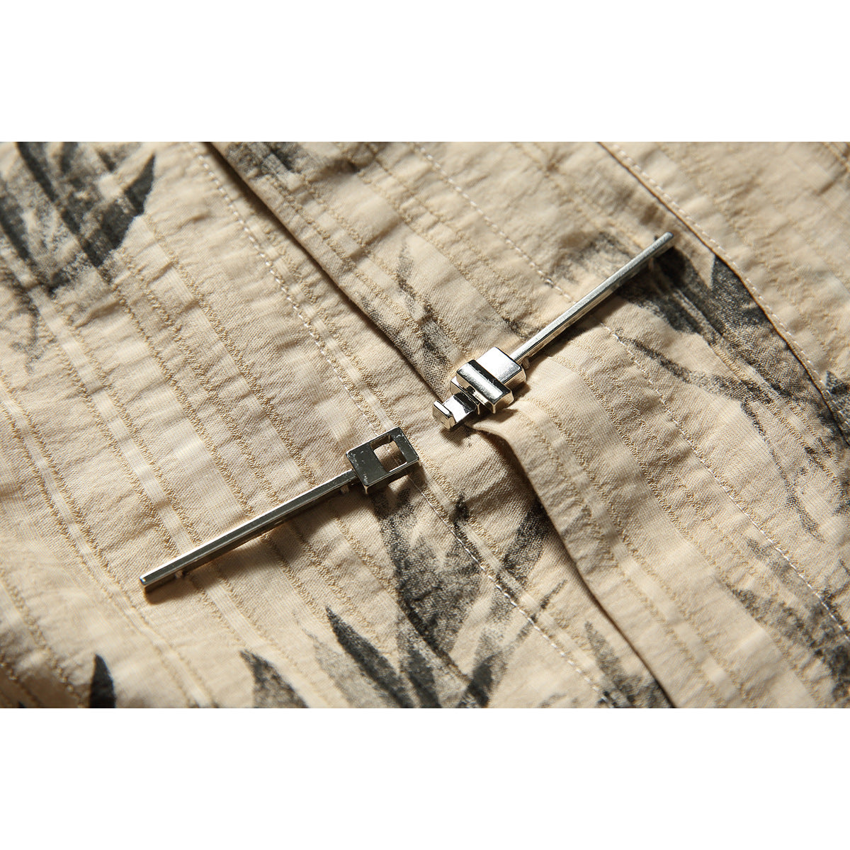 Close-up of a silver clasp on tan fabric with a dark abstract botanical print and visible stitching.