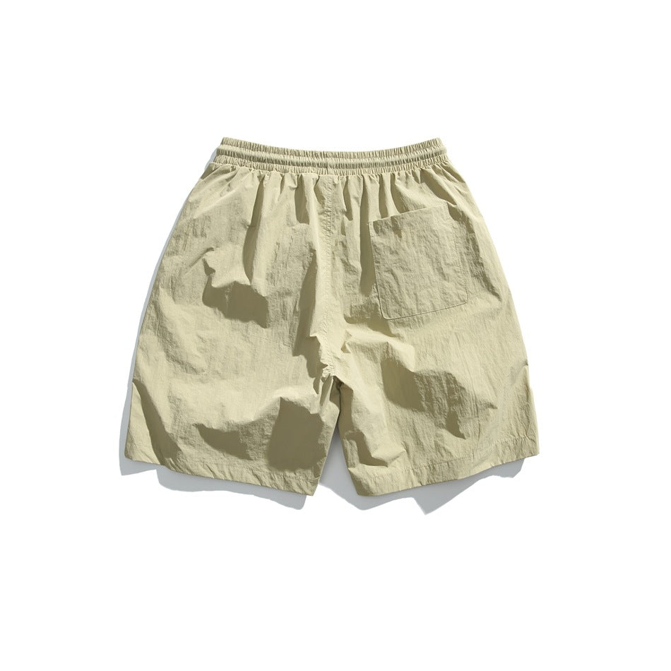 Back view of pale khaki shorts with an elastic waistband, loose legs, and a large patch pocket.
