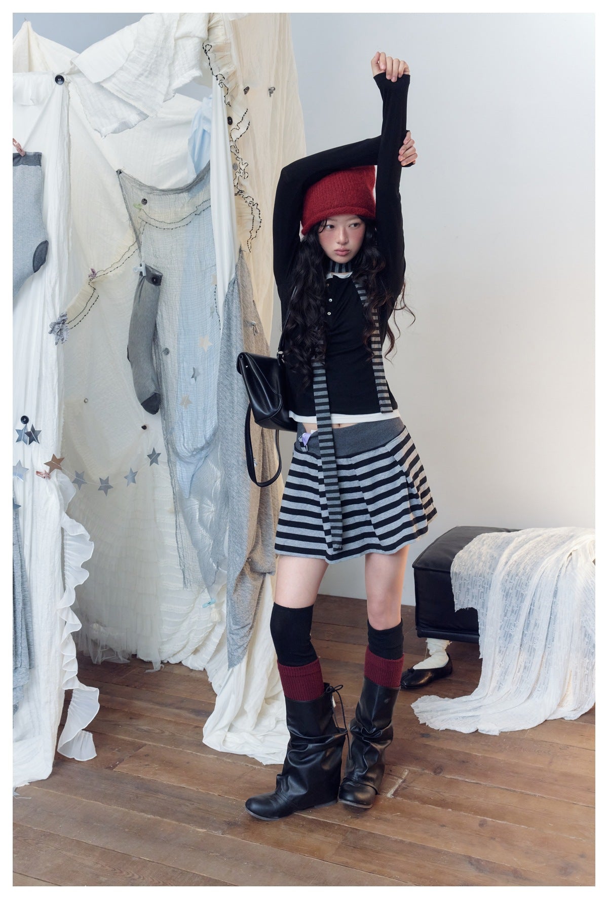 Full-length model wearing a black top, gray-and-black striped mini skirt and scarf, and a red knit hat.