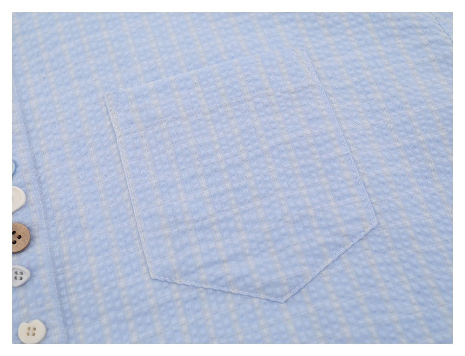 Close-up of a patch pocket on a light blue subtly checked shirt, with several buttons visible at the edge.