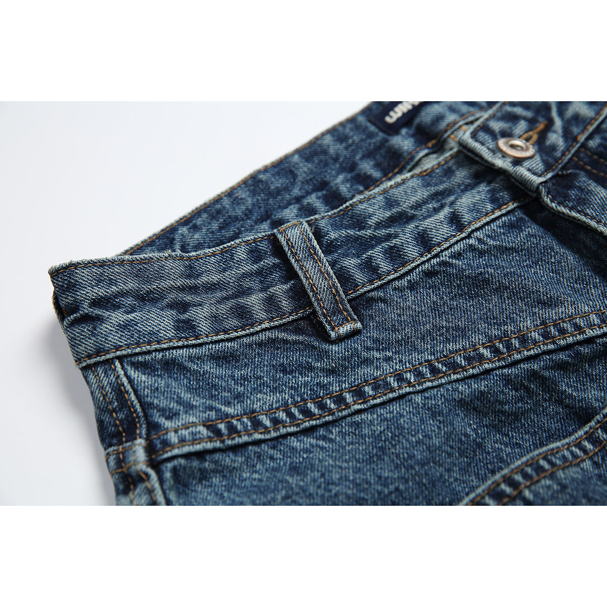 Close-up of blue-wash jeans at the waistband, showing a belt loop, stitching, and metal button.
