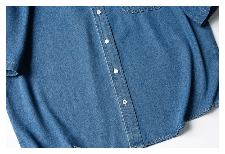 Flat-lay view of the front of a blue denim button-up shirt, with white buttons and a chest pocket.