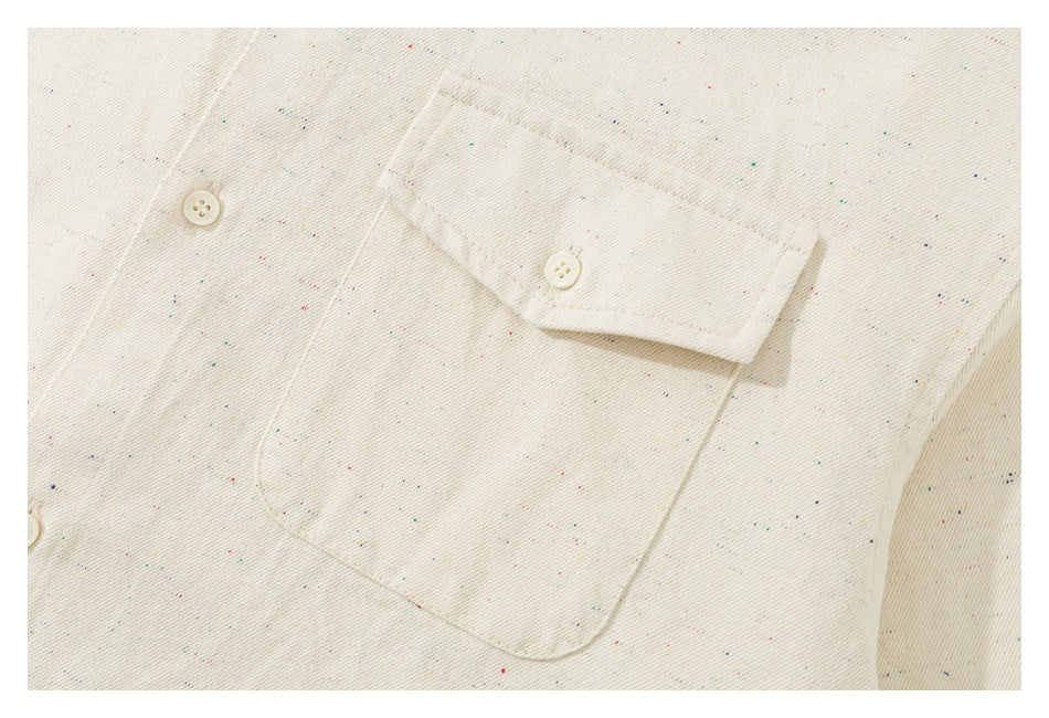 Close-up of an ivory speckled shirt’s buttoned chest pocket and flap.