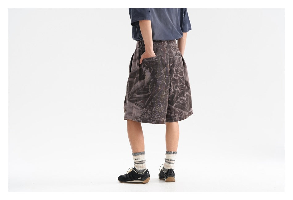 Rear three-quarter view of a model wearing dark gray abstract-print shorts with side pockets and an elastic waist.