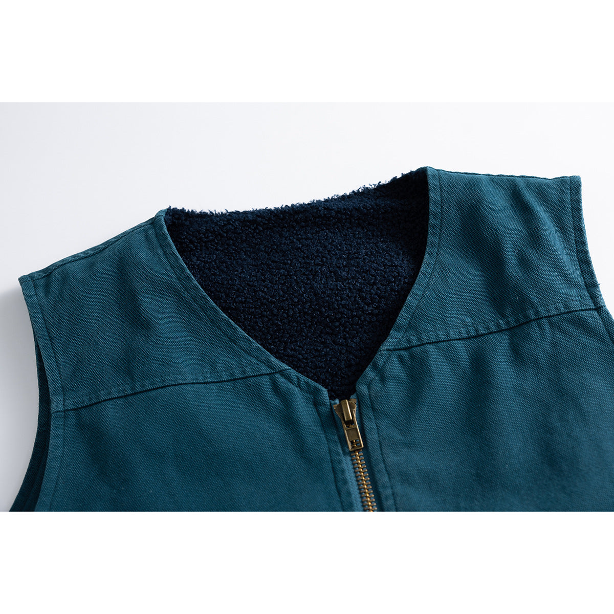 Close-up of a teal sleeveless vest with a V-neck, brass-tone zipper and dark textured lining.