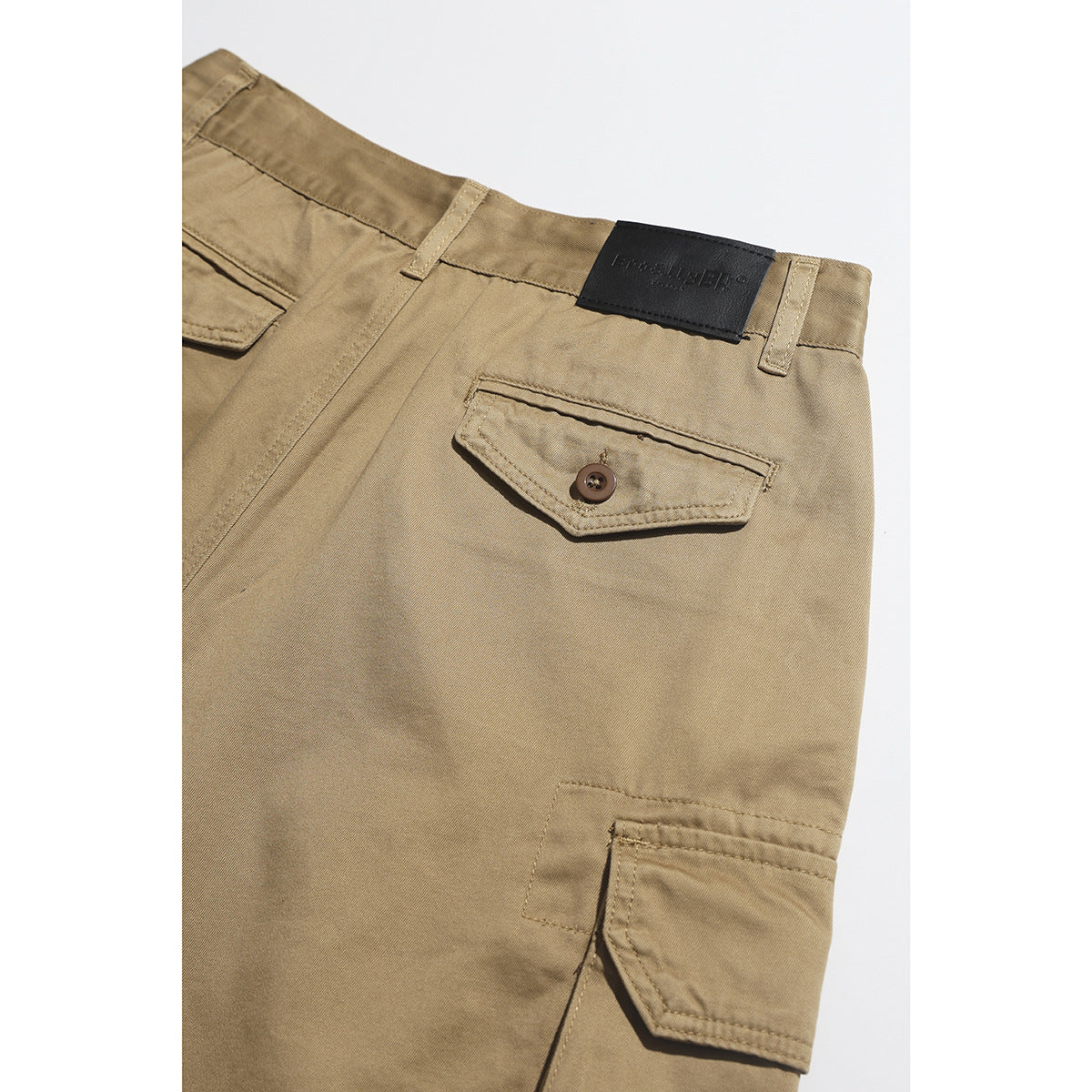 Back detail of tan cargo shorts with buttoned pockets and a black waistband patch.