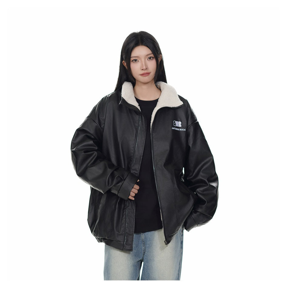 Model wearing an open black oversized jacket with a cream fleece collar and small chest logo over a black top.