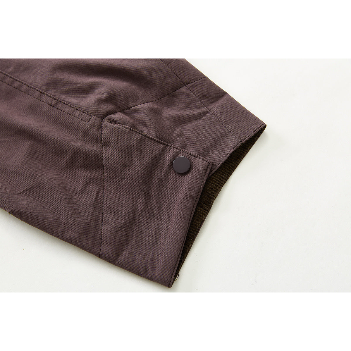 Close-up of a plum jacket cuff with a dark snap button and brown corduroy lining.