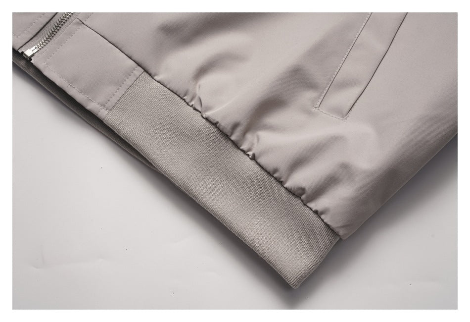Close-up of a light taupe jacket's ribbed hem, gathered fabric, and welt pocket.