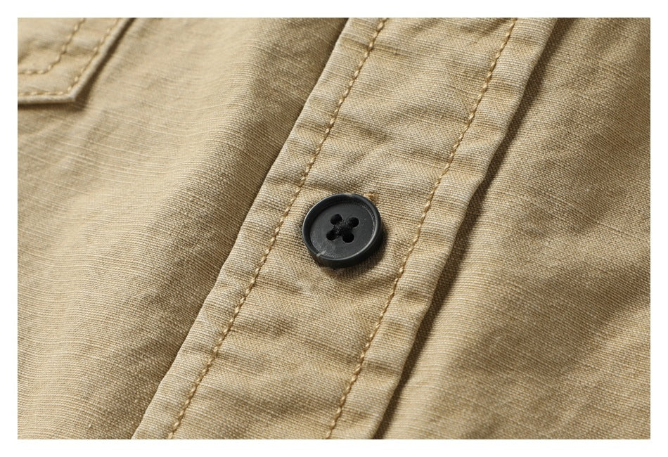 Close-up of tan garment fabric with a black four-hole button and parallel stitched seams.
