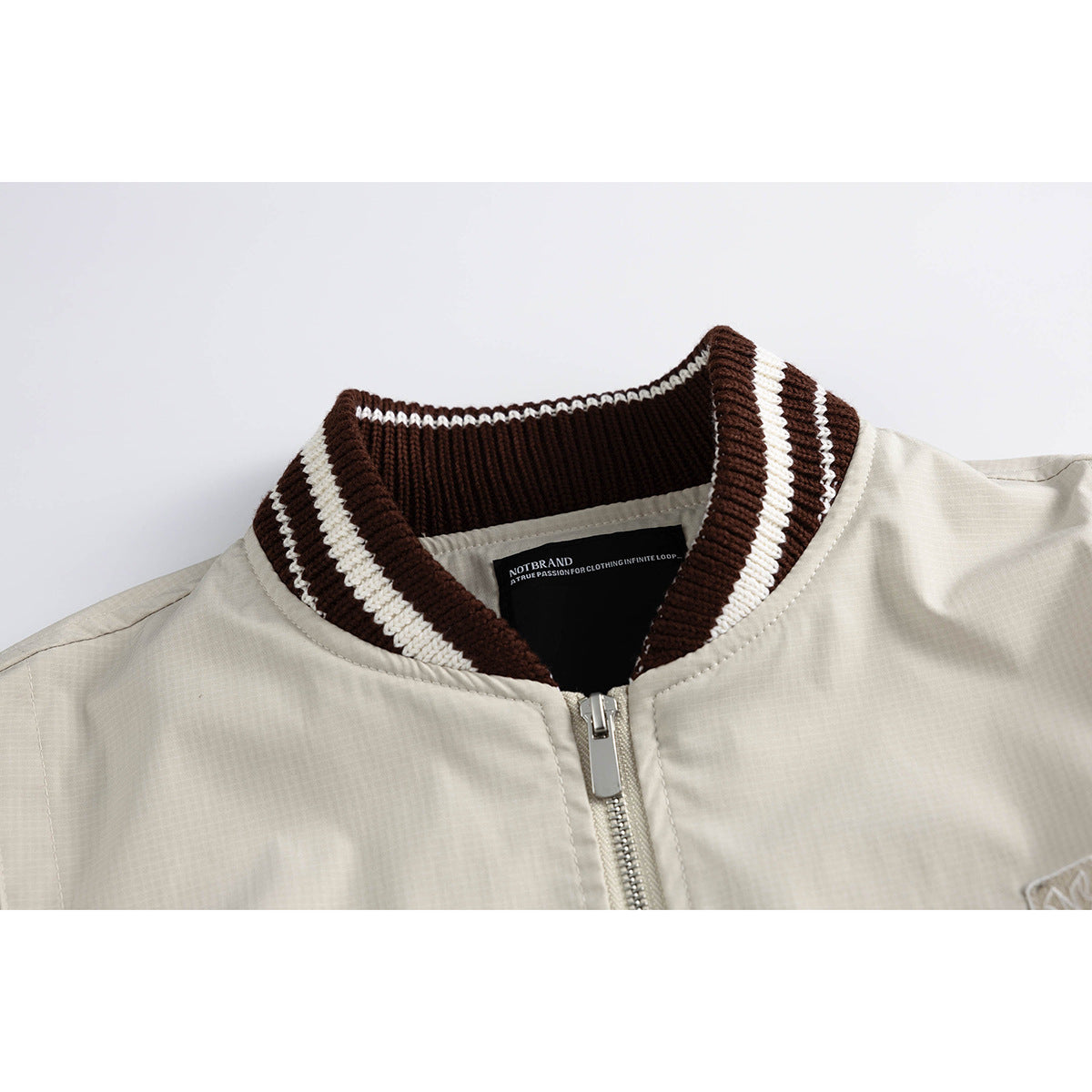 Close-up of a light beige zip jacket with a dark brown and cream striped ribbed collar.