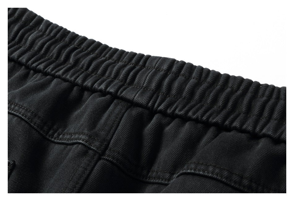 Close-up of black pants showing a gathered elastic waistband and stitched seams.