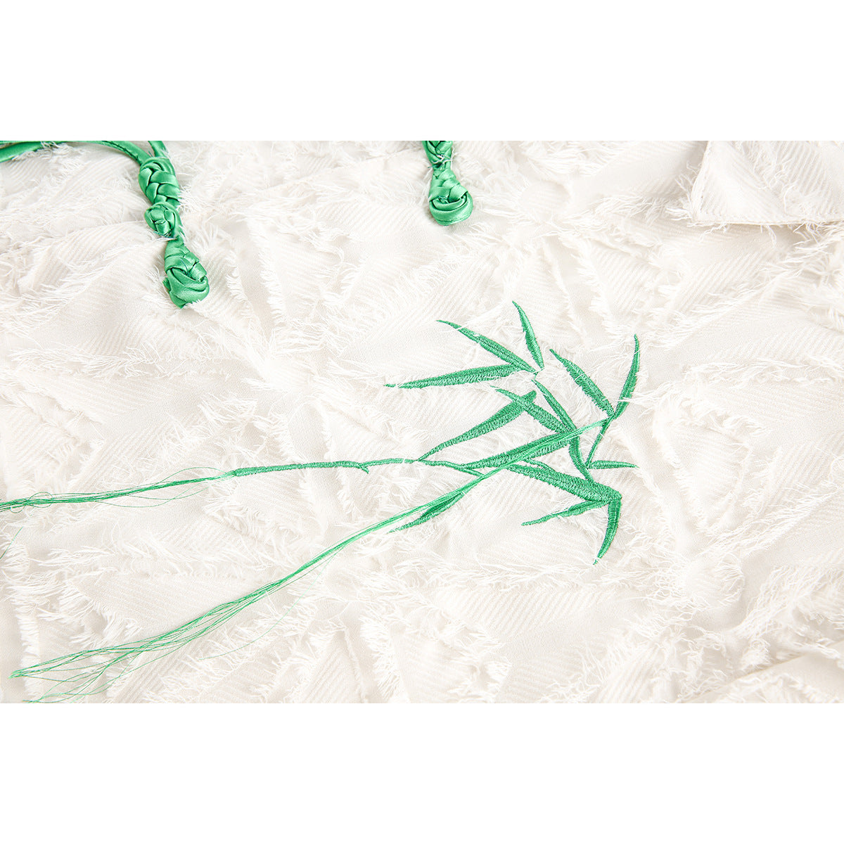 Green bamboo embroidery and braided cord closures on white textured fabric.