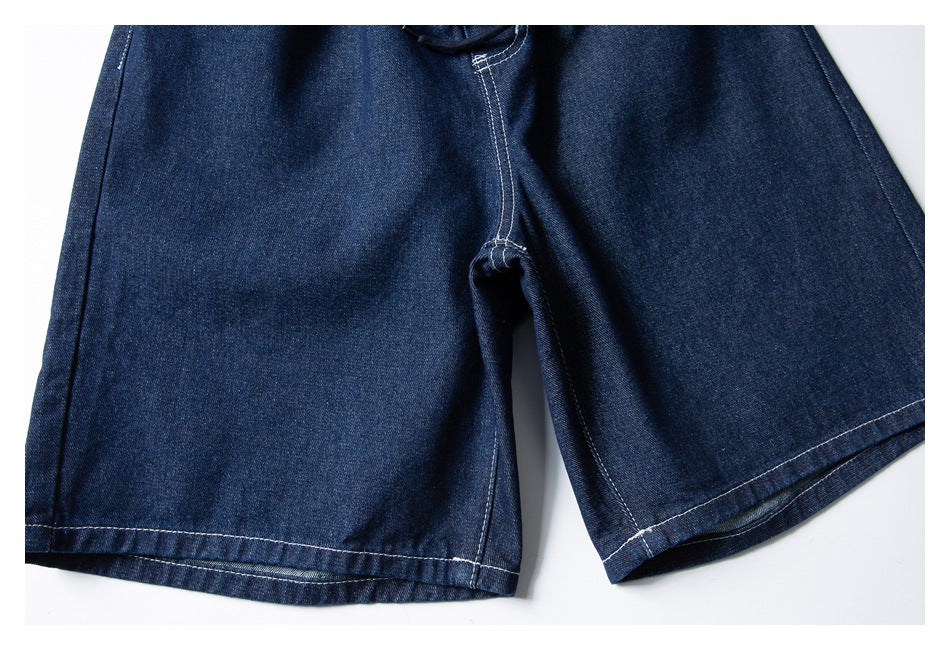 Close-up of dark indigo denim shorts showing the crotch seam and wide leg hems with white stitching.