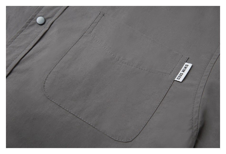 Close-up of the gray shirt's front patch pocket, snap button, and small SWIM SEED label.