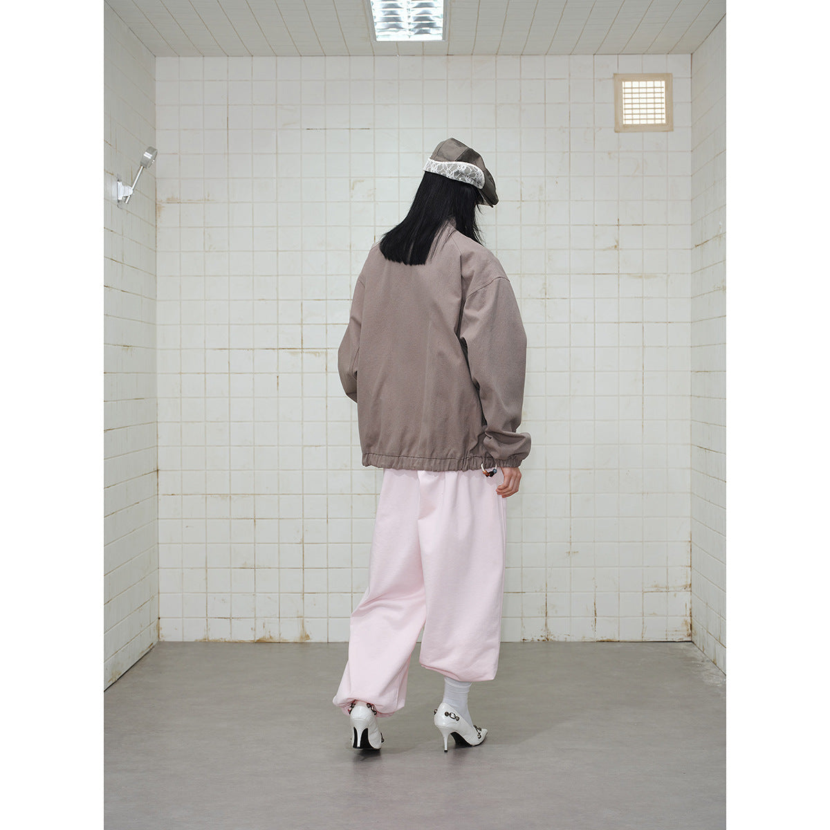 Rear view of a model wearing an unprinted taupe jacket with elastic cuffs and hem, and pale pink pants.