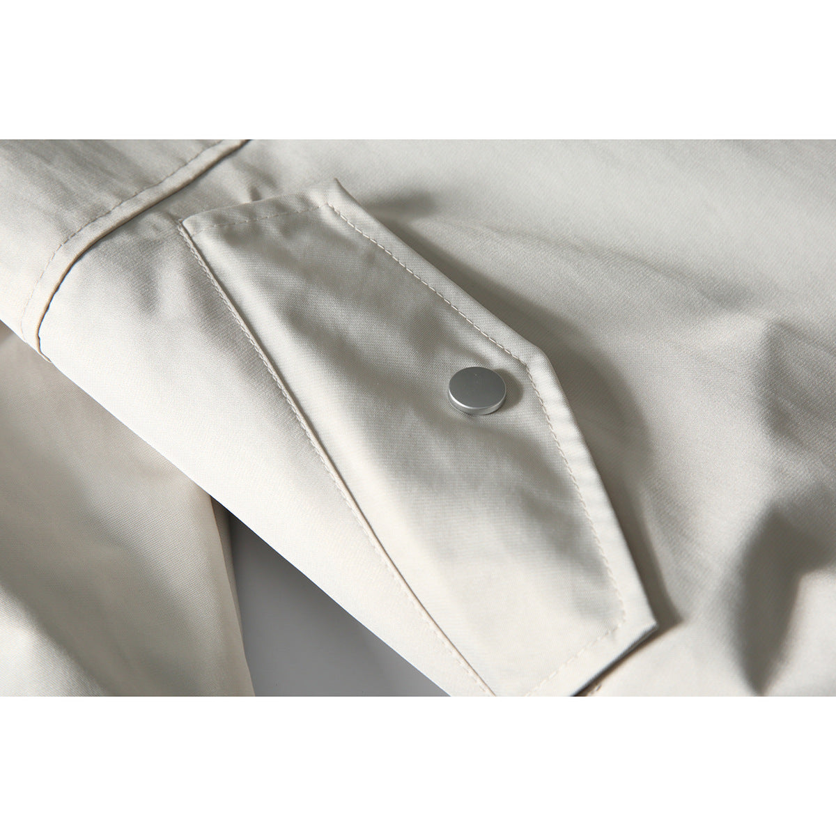 Close-up of an ivory jacket's flap and single silver snap button.