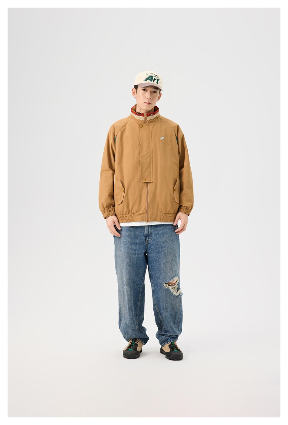 Full-length front view of a model wearing a tan jacket with dark teal accents and relaxed blue distressed jeans.