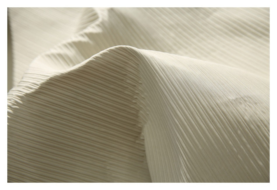 Close-up highlighting the fine ridged pleats and folds of ivory garment fabric.
