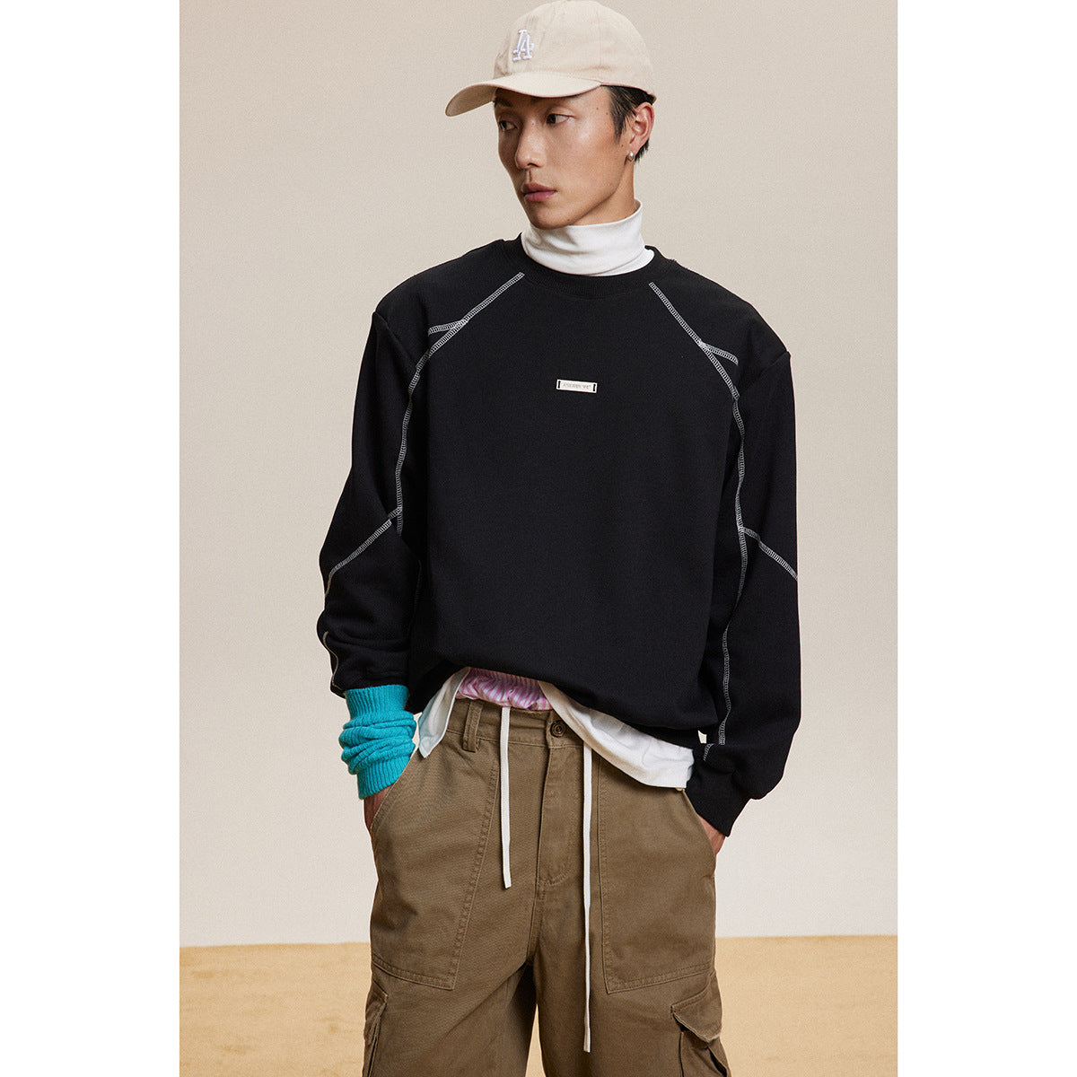 Front view of a model wearing a black sweatshirt with light contrast seams and a small chest label.