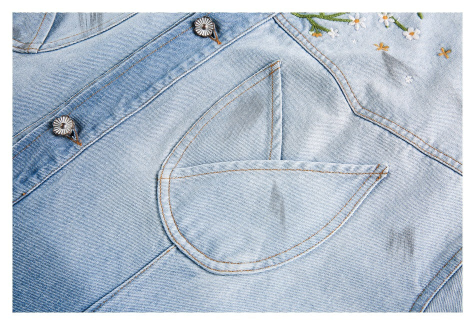 Close-up of a curved chest pocket and decorative metal buttons on a light-wash denim jacket.