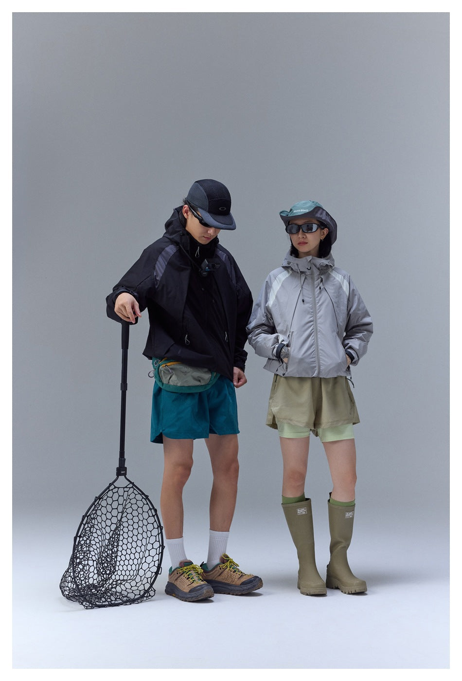 Two models in outdoor clothing: black and silver hooded jackets with teal and khaki shorts, posed with fishing gear.