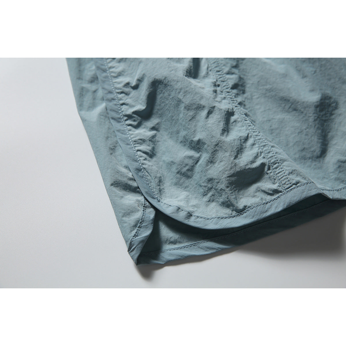 Close-up of the curved hem and stitched panels on a blue-gray skirt.