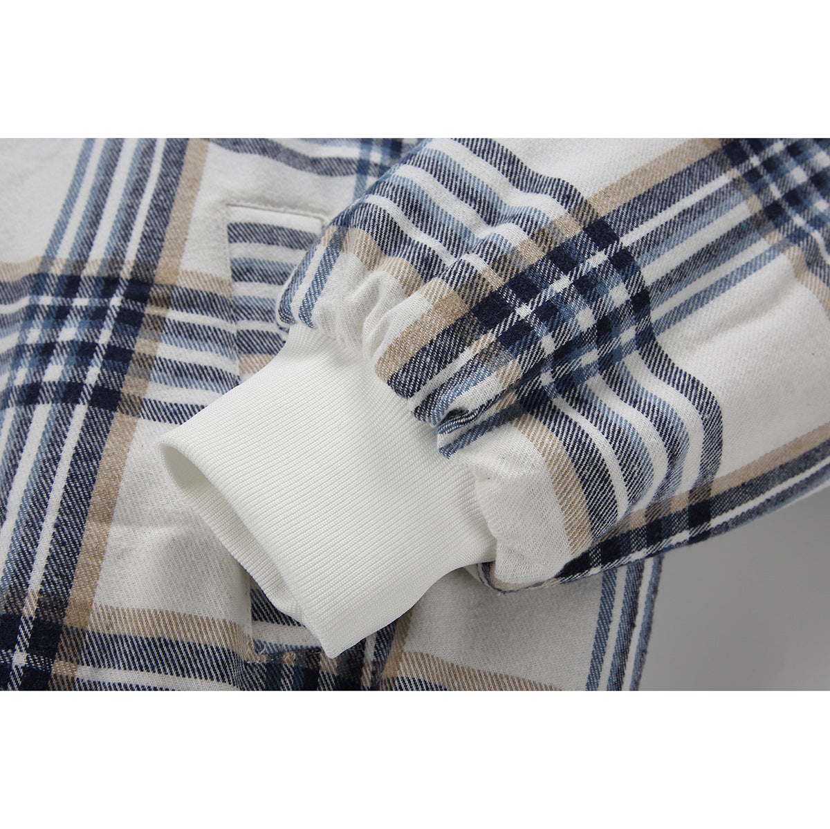 Close-up of a white ribbed cuff on a cream, navy, and tan plaid jacket sleeve.