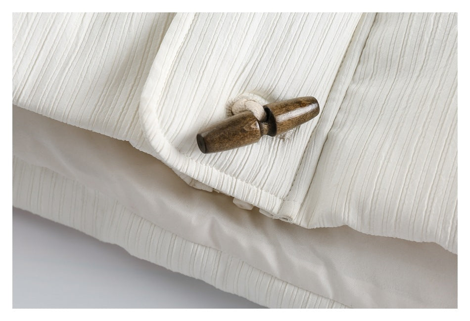 Close-up of an ivory ribbed garment with a brown wooden toggle fastener.